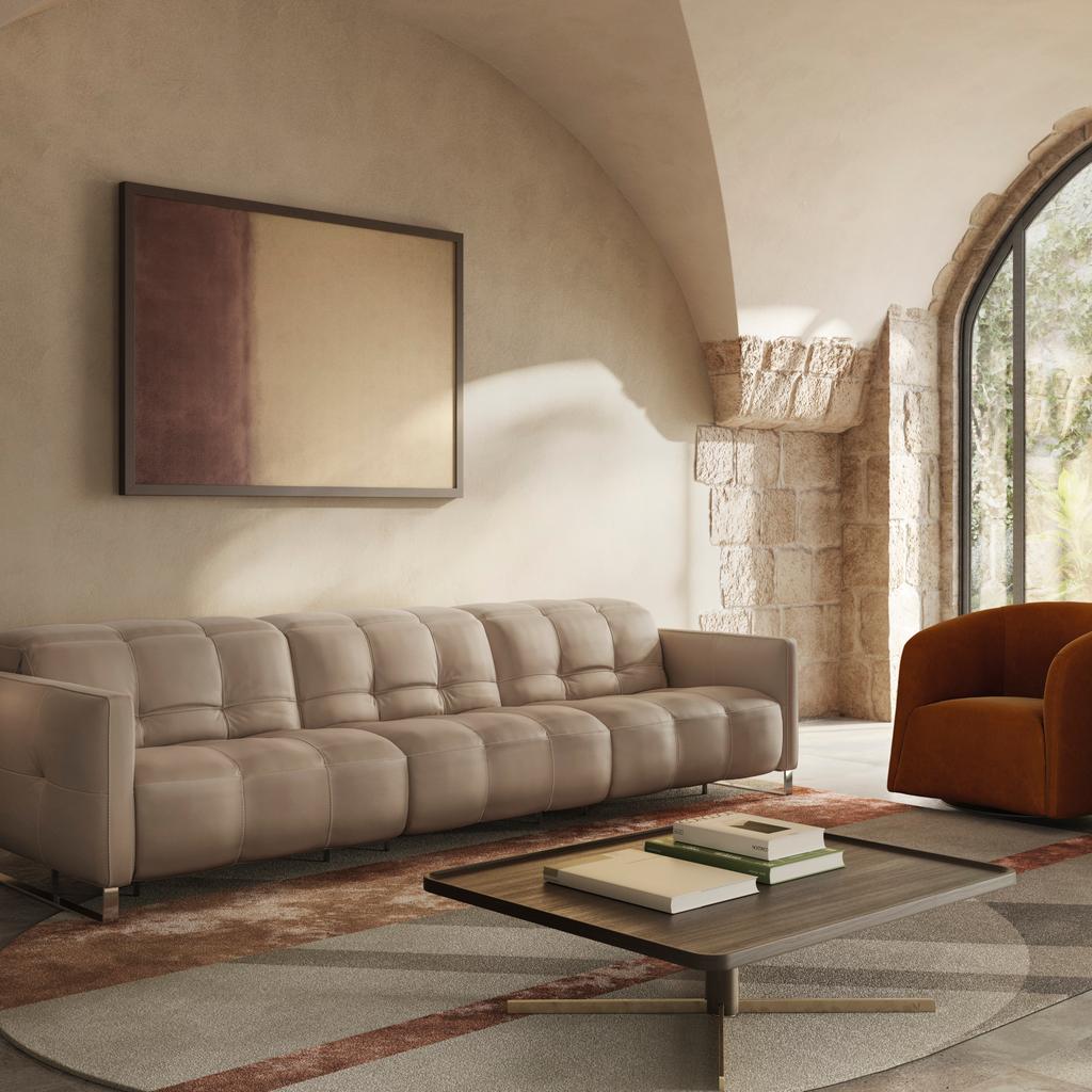 The Fero sofa, also known as the Natuzzi Philo, is presented in a warm beige leather finish within a softly lit, architectural living space. Featuring deep, structured cushioning and clean lines, this modern Italian sofa is styled with accent chairs and a
