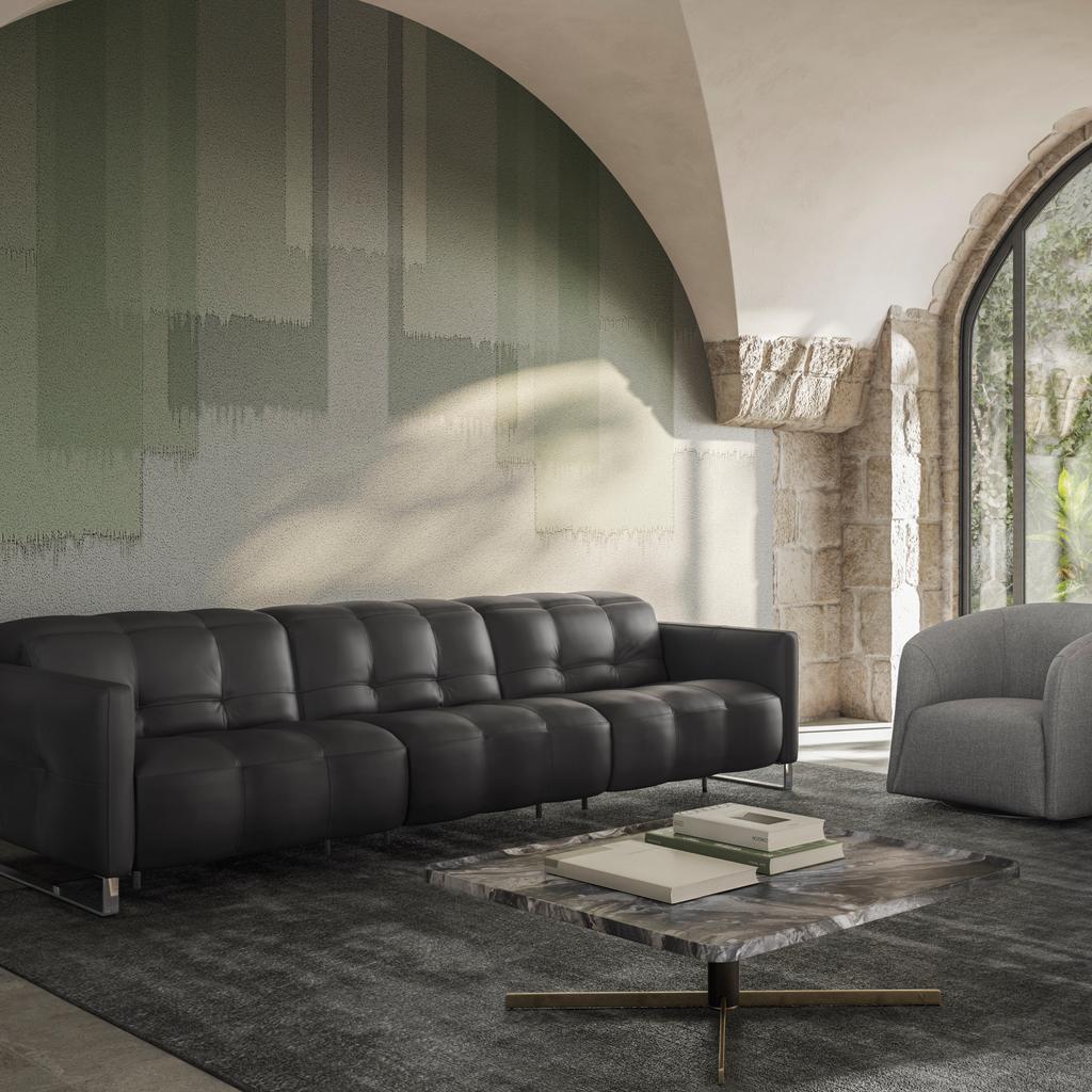This image features the Fero sofa, known as the Natuzzi Philo, upholstered in rich dark leather and styled against a textured green wall. The sofa’s deep tufted seating and refined proportions create a bold yet elegant statement, complemented by modern fu