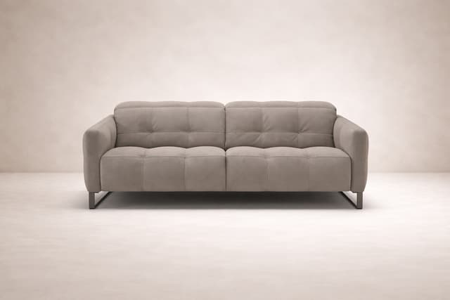 Front view of the Fero sofa, known as the Natuzzi Philo, upholstered in soft beige fabric and presented against a minimal, neutral backdrop. The design features deep, structured cushioning, subtle tufted detailing, and slim metal legs, reflecting modern I