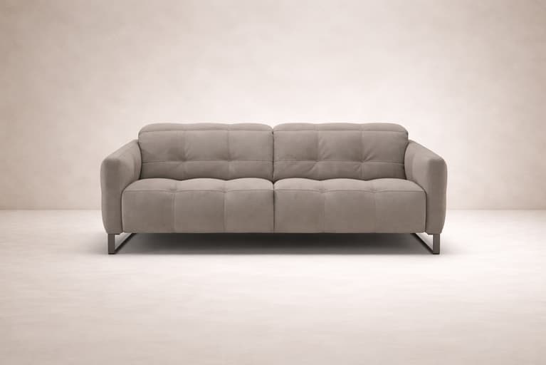 Front view of the Fero sofa, known as the Natuzzi Philo, upholstered in soft beige fabric and presented against a minimal, neutral backdrop. The design features deep, structured cushioning, subtle tufted detailing, and slim metal legs, reflecting modern I