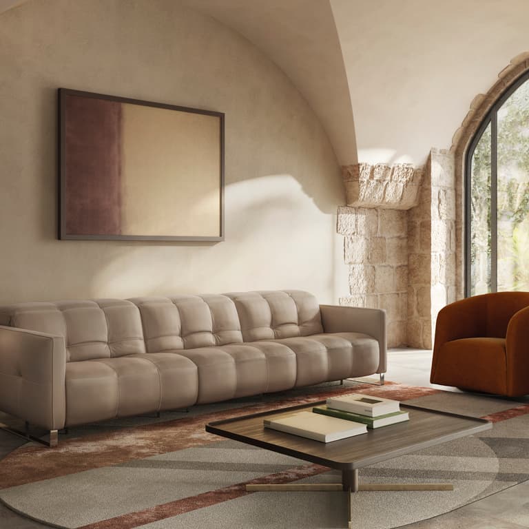 The Fero sofa, also known as the Natuzzi Philo, is presented in a warm beige leather finish within a softly lit, architectural living space. Featuring deep, structured cushioning and clean lines, this modern Italian sofa is styled with accent chairs and a