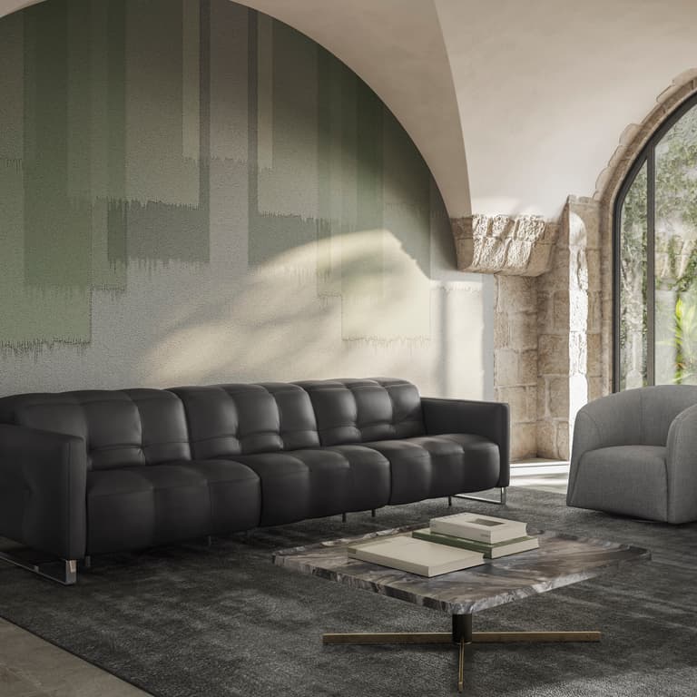 This image features the Fero sofa, known as the Natuzzi Philo, upholstered in rich dark leather and styled against a textured green wall. The sofa’s deep tufted seating and refined proportions create a bold yet elegant statement, complemented by modern fu